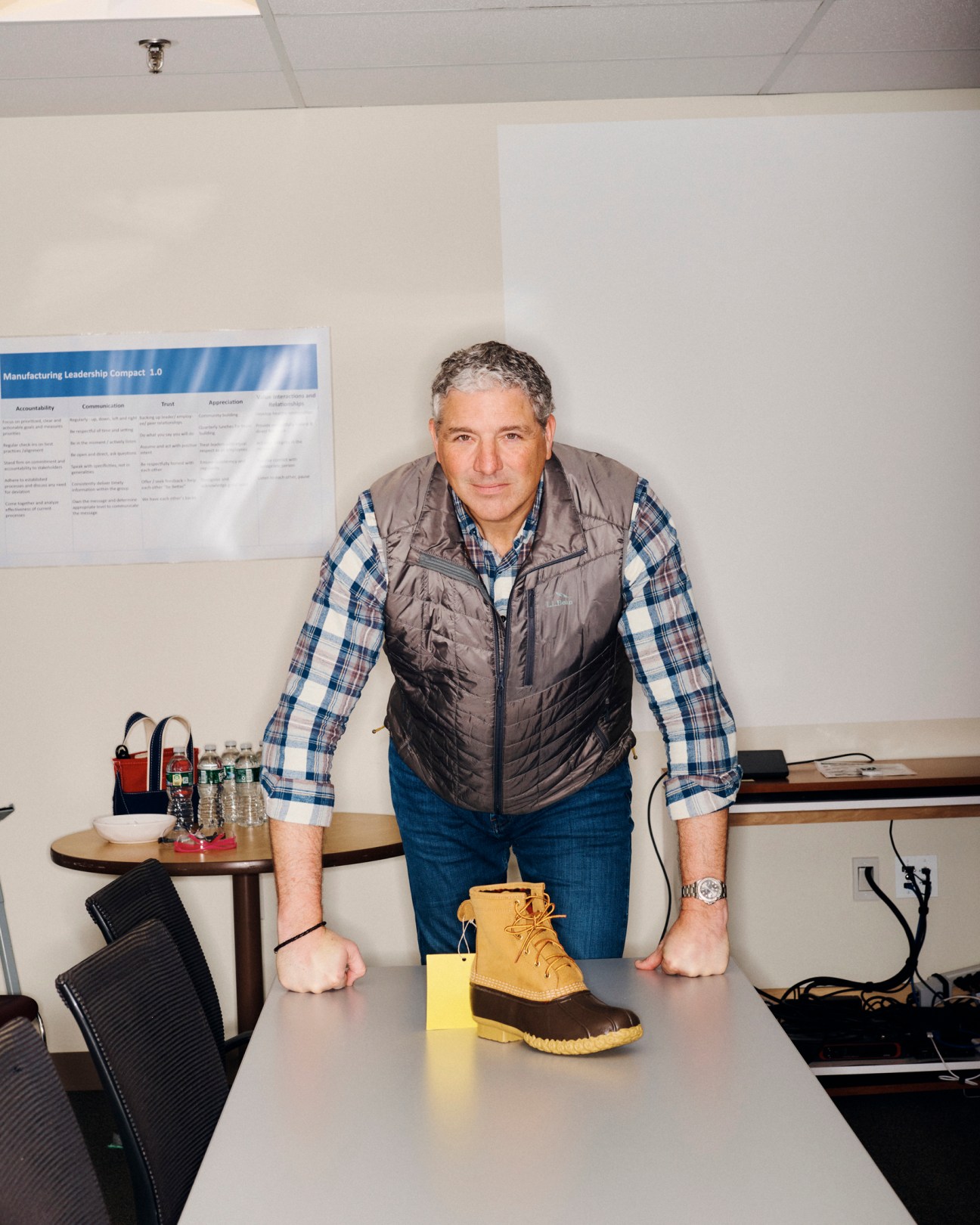Shawn Gorman in grey vest and plaid shirt standing behind desk with Bean Boot