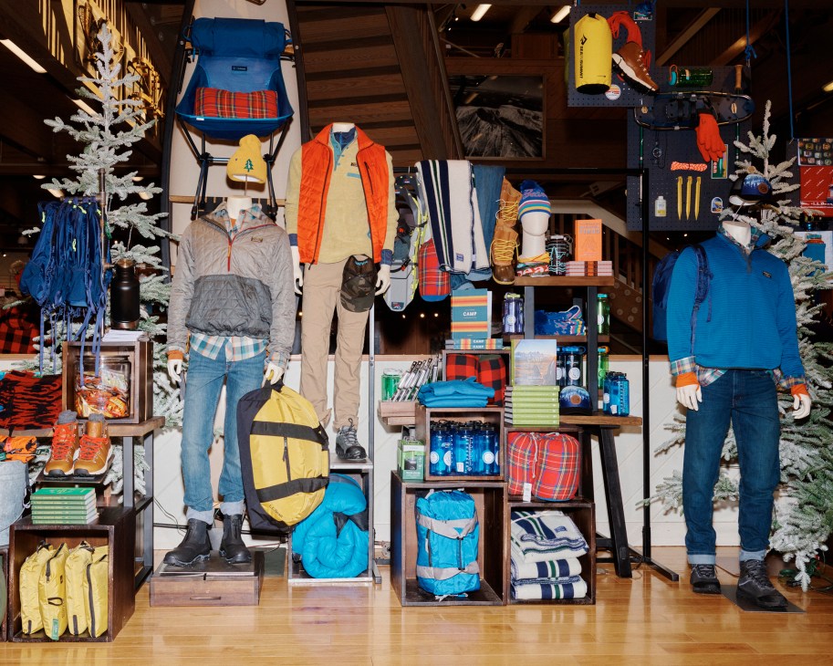 Outdoor retail store display with mannequins wearing hiking gear, camping equipment, and colorful backpacks on shelves