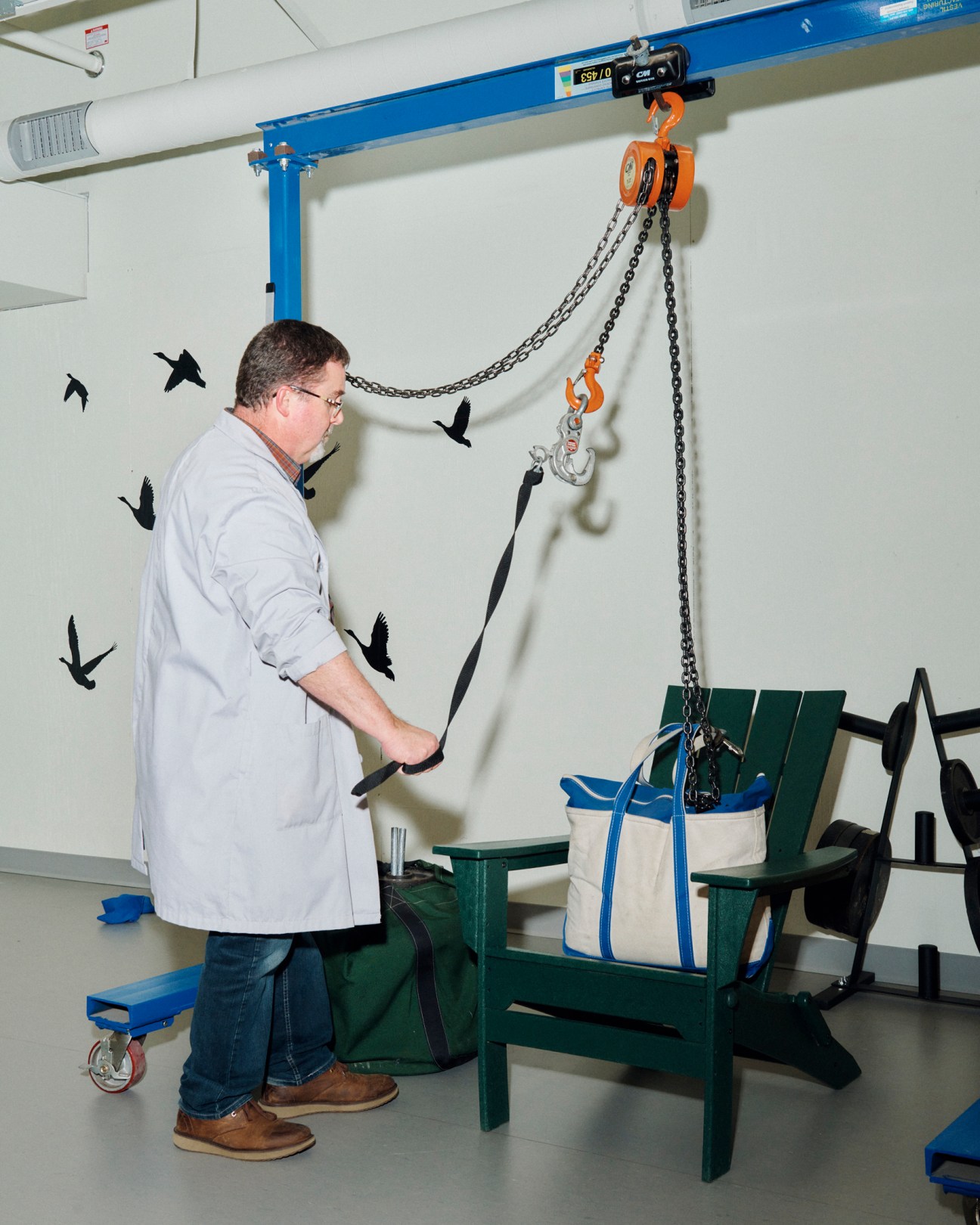 Man in white lab coat operating chain hoist to test tote bag durability in testing facility