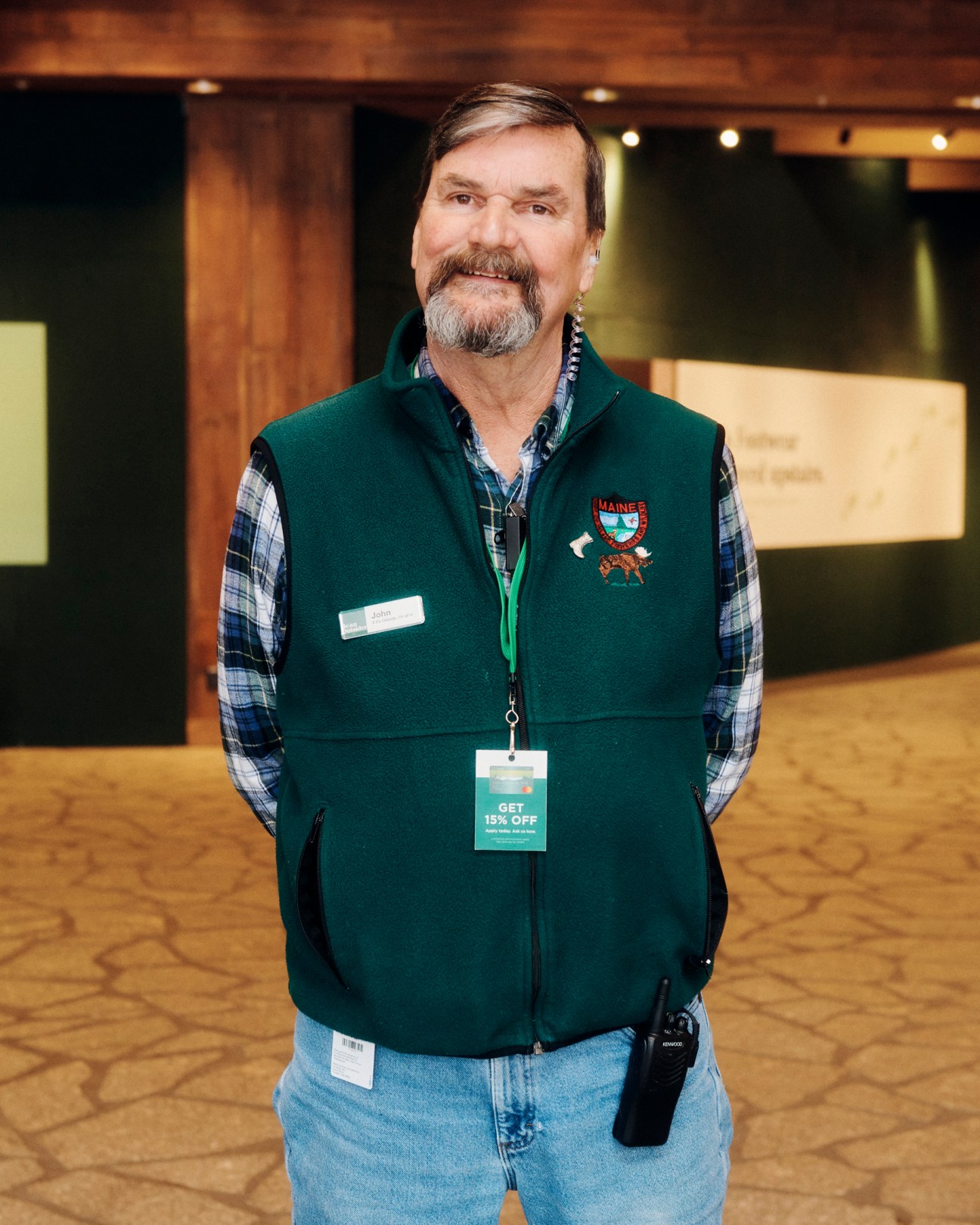 Man in green vest and plaid shirt with name tag standing in retail store interior