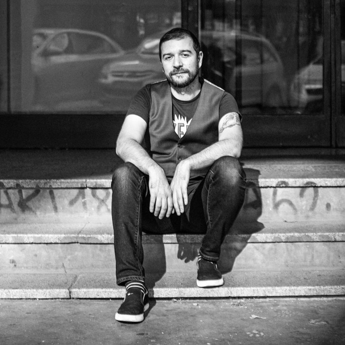 Portrait of Stevan Dojcinovic sitting on stone steps in black and white