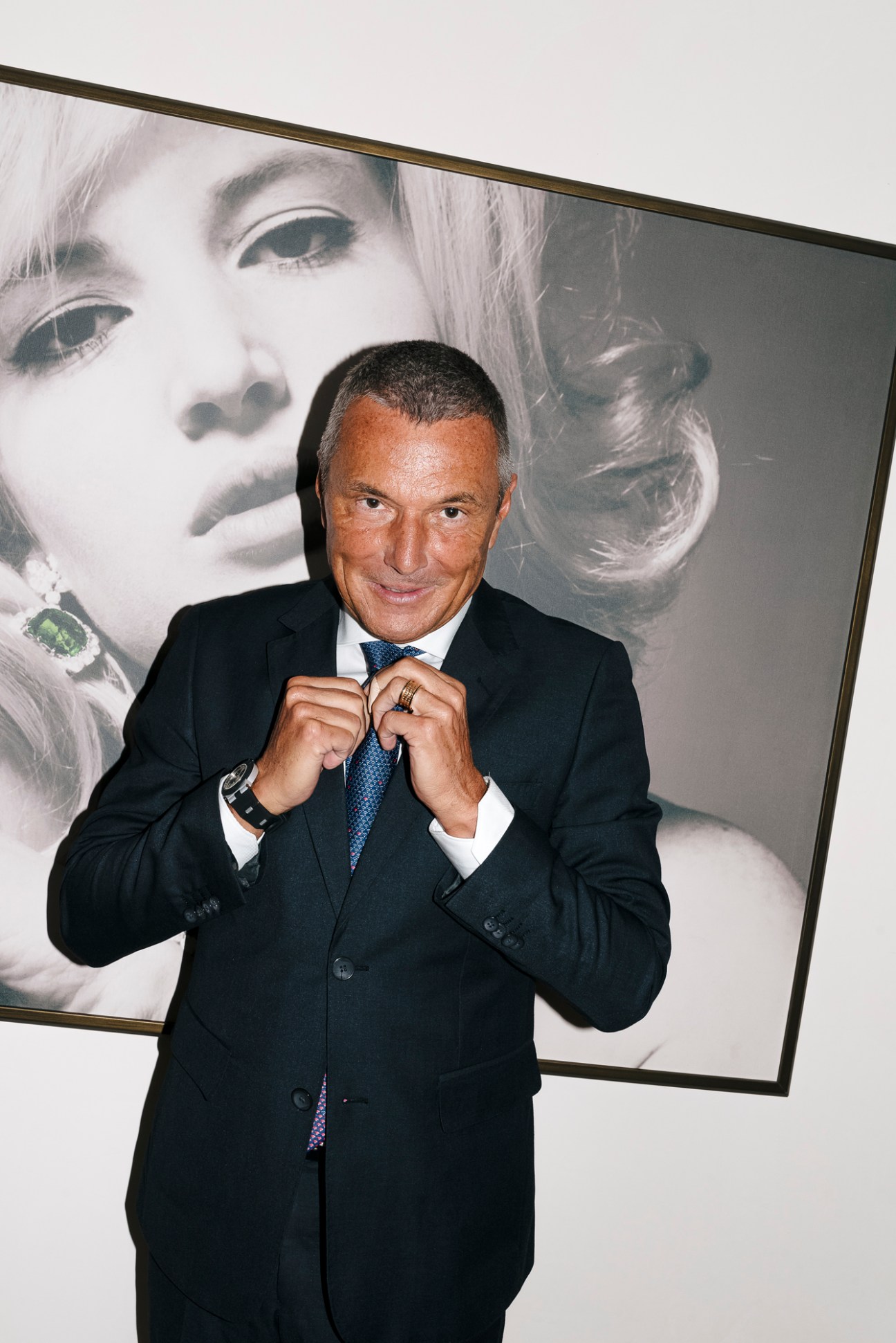 Jean-Christophe Babin adjusting his tie while standing in front of a large black and white portrait