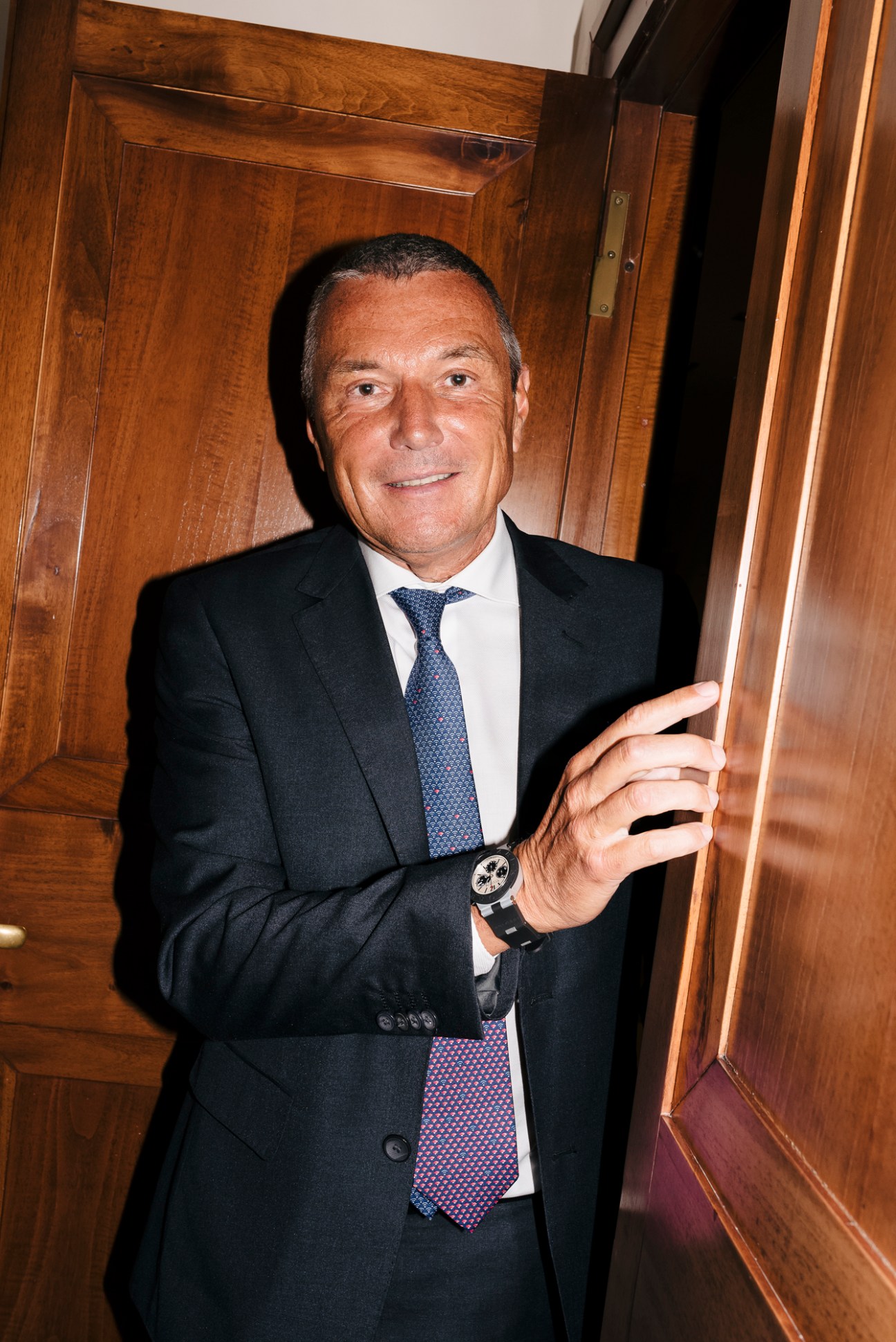 Jean-Christophe Babin, CEO of Bulgari, wearing a dark suit and tie, standing by wooden cabinetry