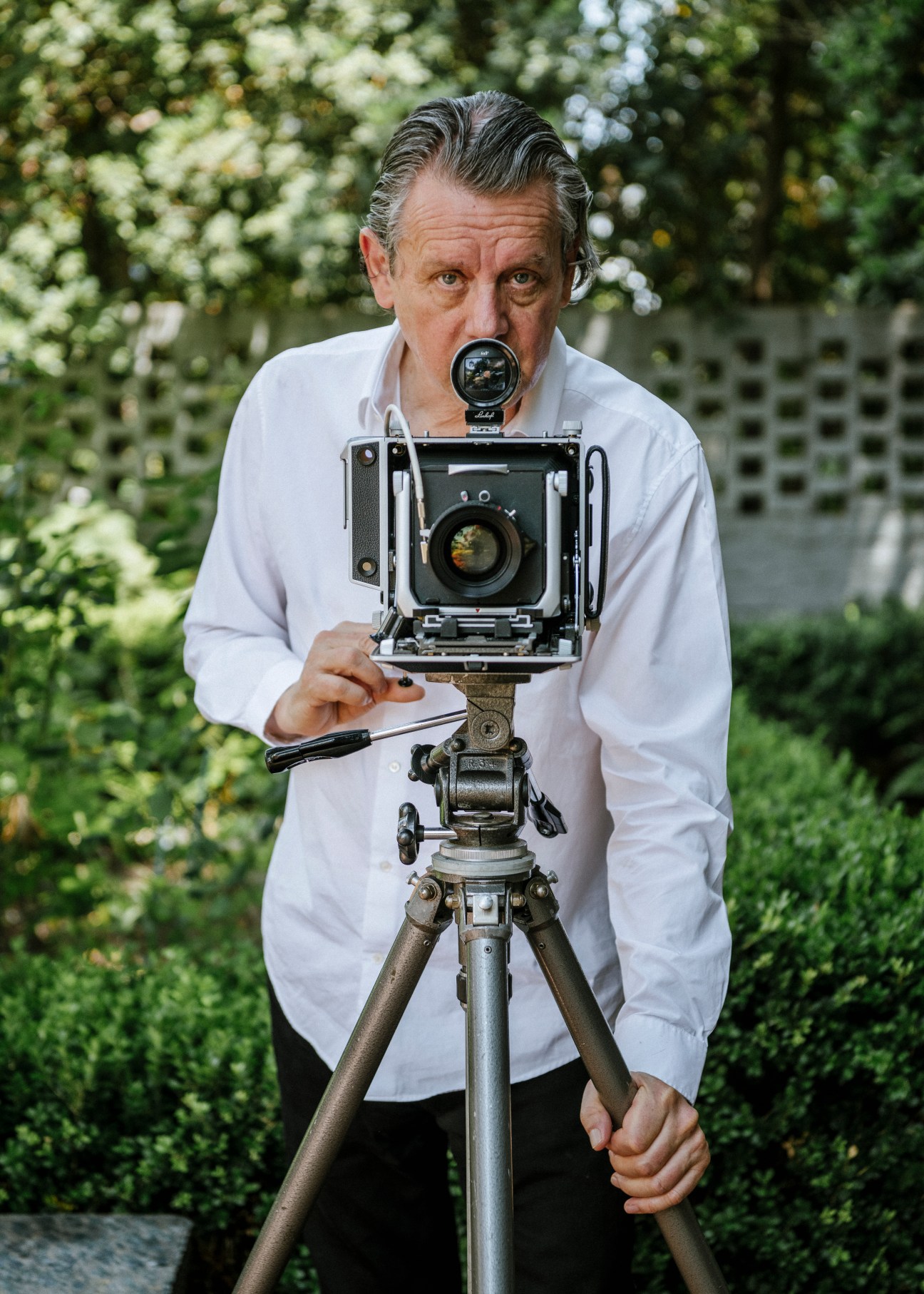 Jeff Wall looking through a large format camera mounted on a tripod outdoors