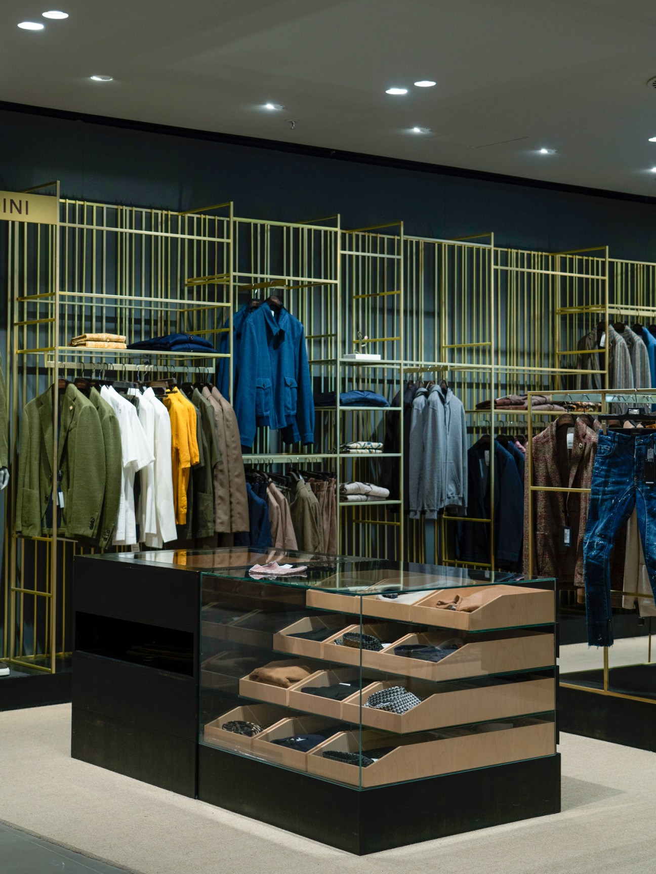 Modern menswear store interior with gold metal grid shelving displaying colorful clothing and wooden display fixtures