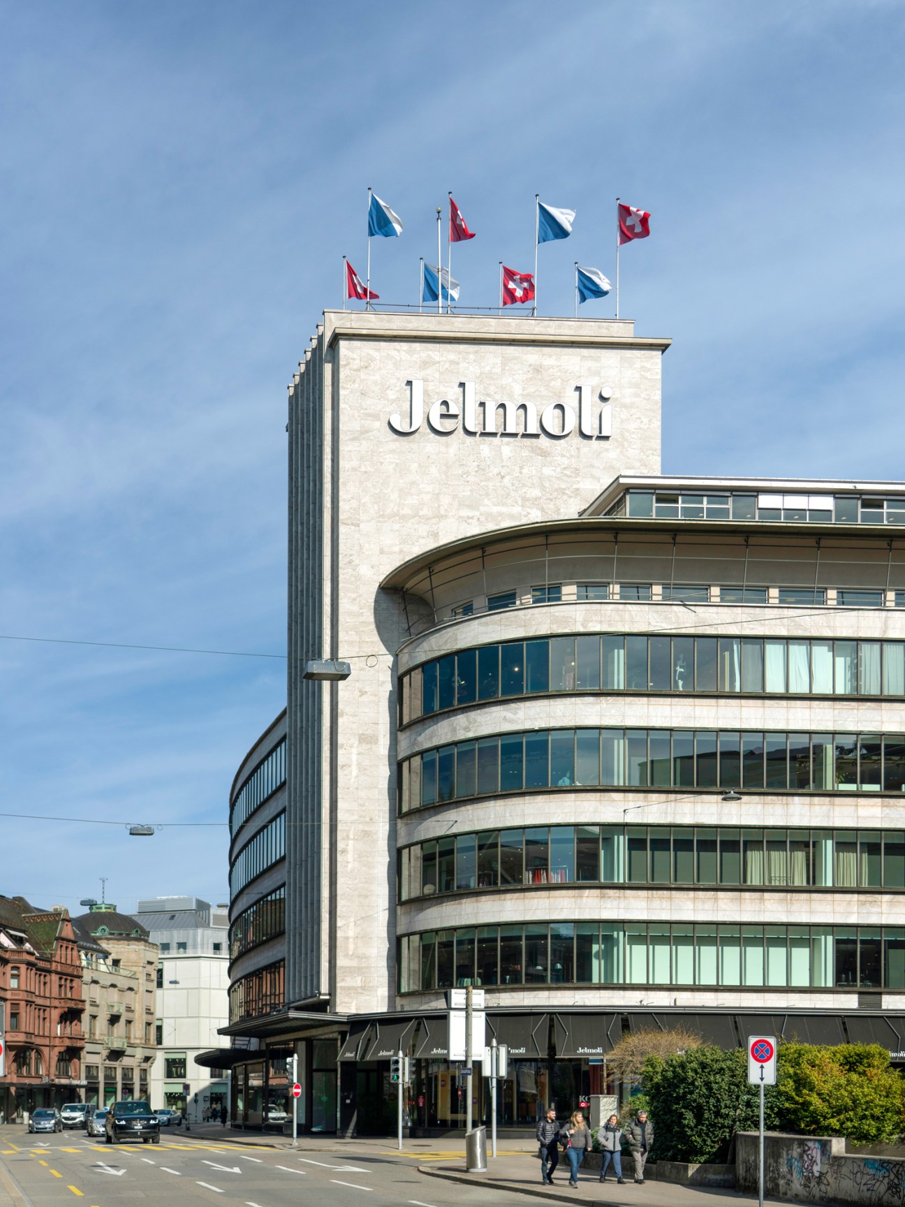 Modern department store exterior with curved glass facade and international flags on rooftop