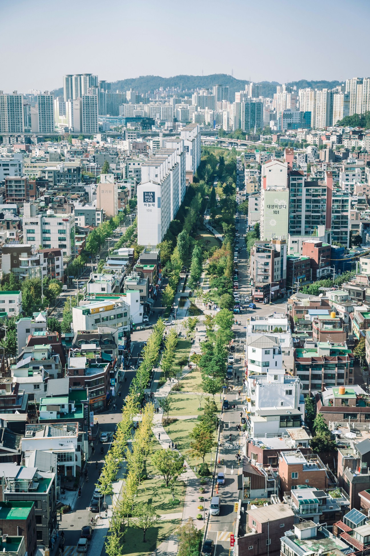Linear park in Seoul with people walking along landscaped path between modern apartment buildings