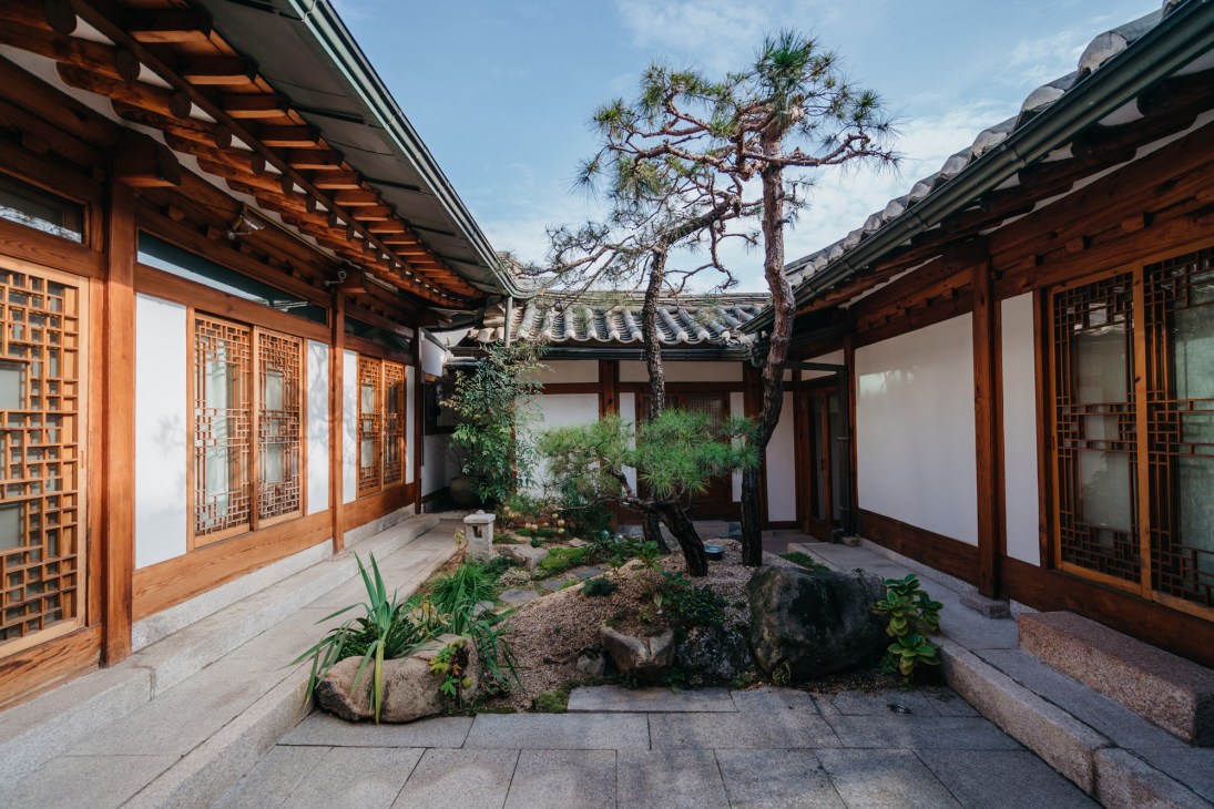 Traditional Korean courtyard with wooden buildings, latticed windows, garden with pine tree and stone elements