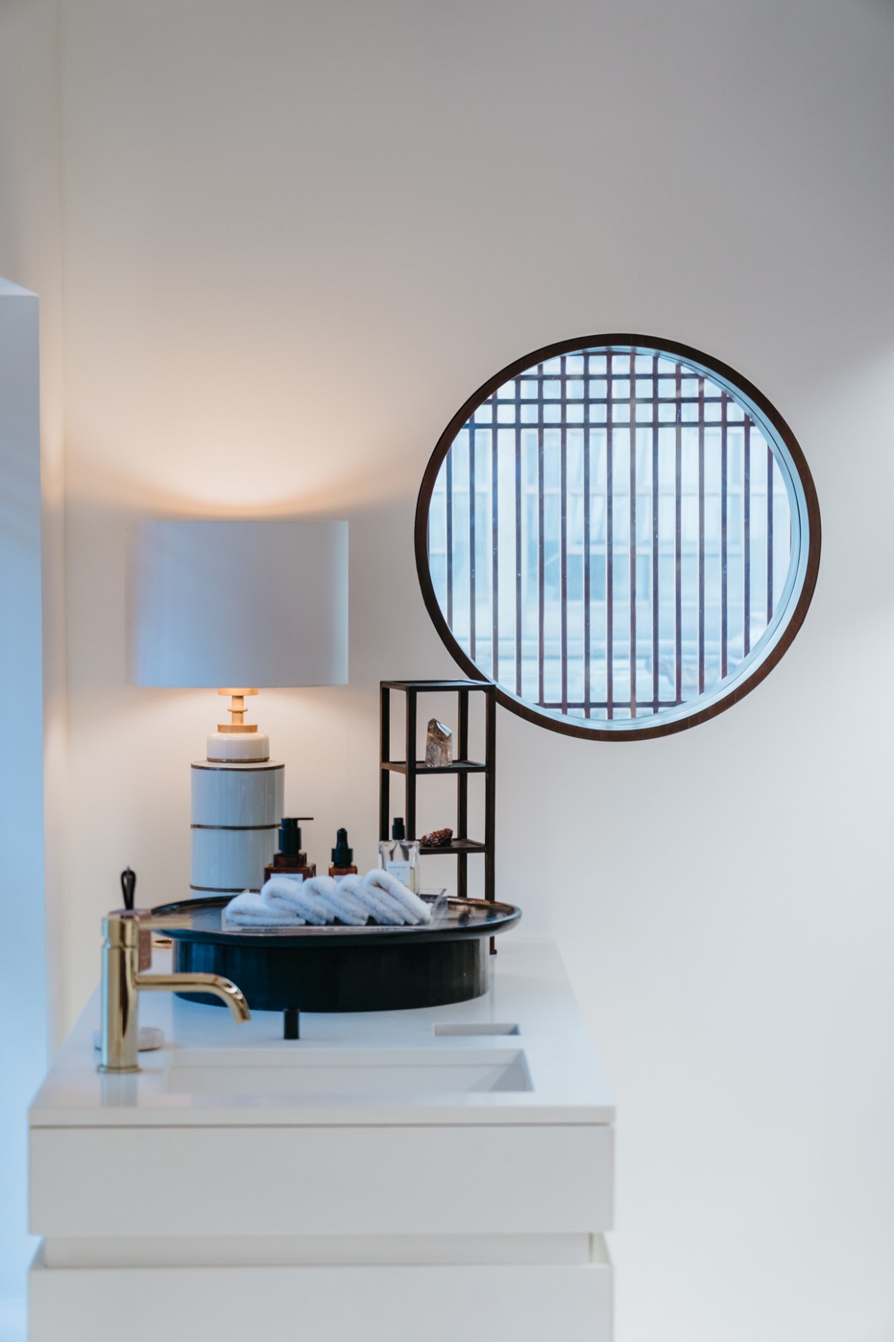 Modern minimalist bathroom with circular mirror, black vessel sink, white walls and natural lighting