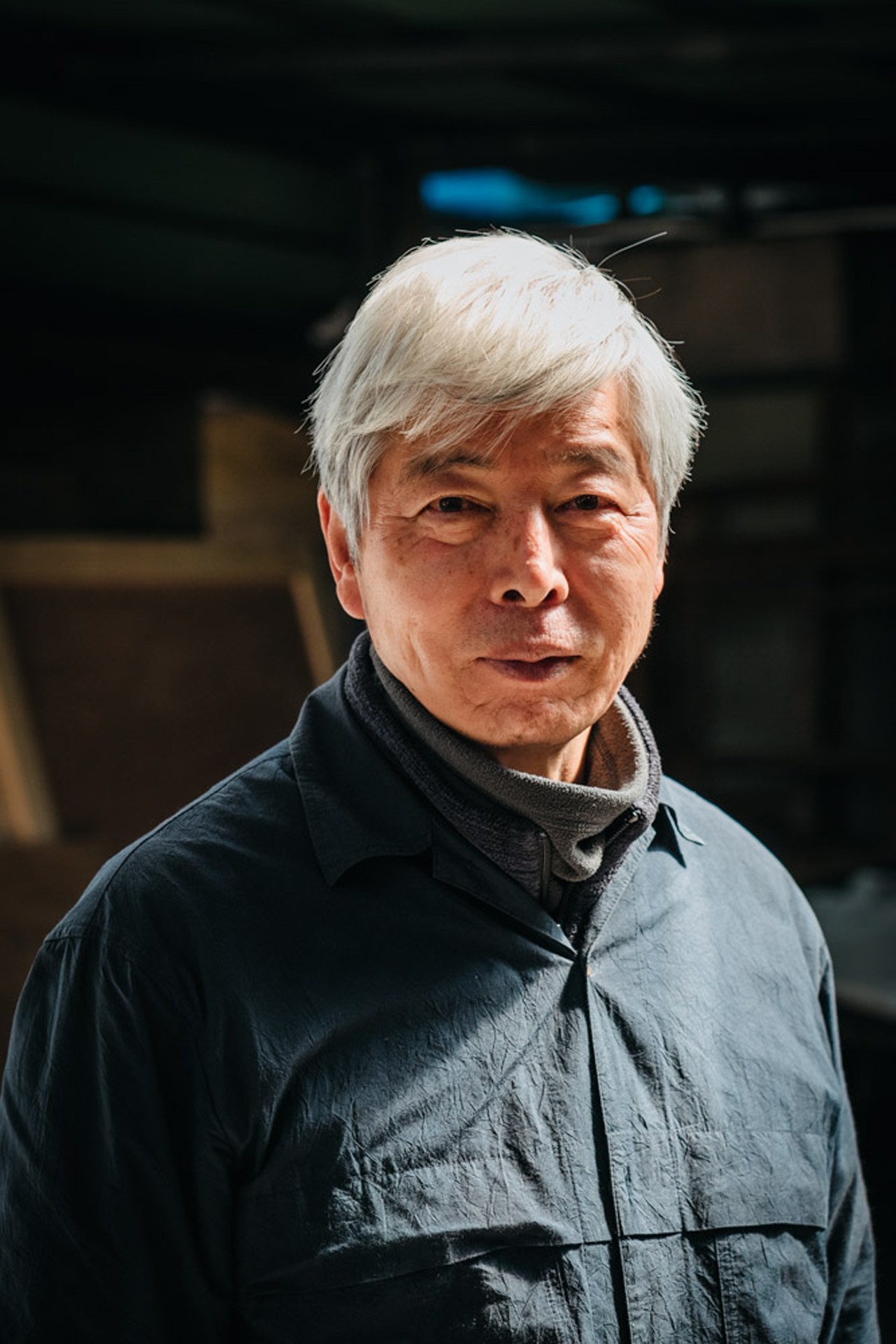 Portrait of Lee Bae, a South Korean artist with white hair wearing a dark jacket.