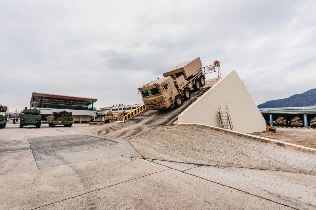 A tan military truck climbing a steep concrete ramp at Hanwha Aerospace facility in South Korea.