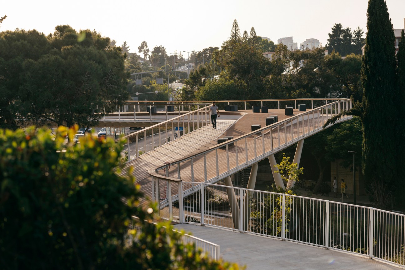 Pedestrian bridge with wooden deck, metal railings, and seating areas overlooking Haifa bay and surrounding landscape.