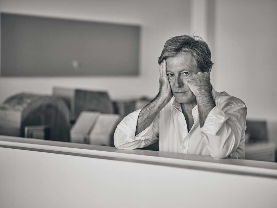 John Pawson, minimalist architect, rests his head on his hand in a contemplative pose at a desk.