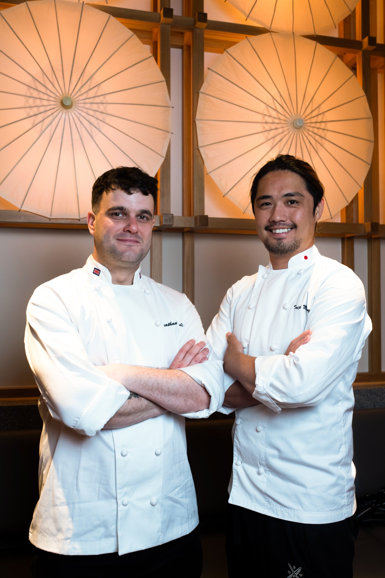 Two chefs in white chef's coats stand together beneath illuminated shoji-paper umbrellas at Taka restaurant in London.