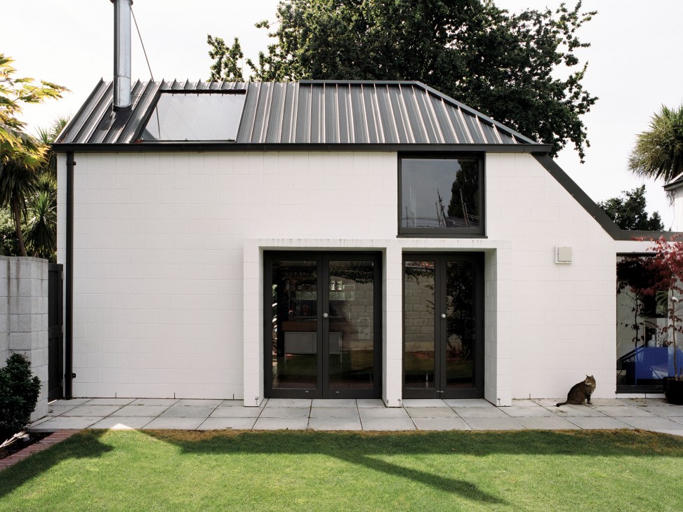 Modern white concrete block house with metal roof and large glass doors, viewed from courtyard garden