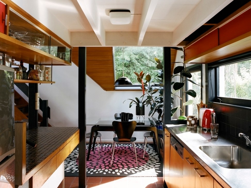 Original galley kitchen with wood cabinets, stainless steel countertops, and black tile backsplash in B Jones house