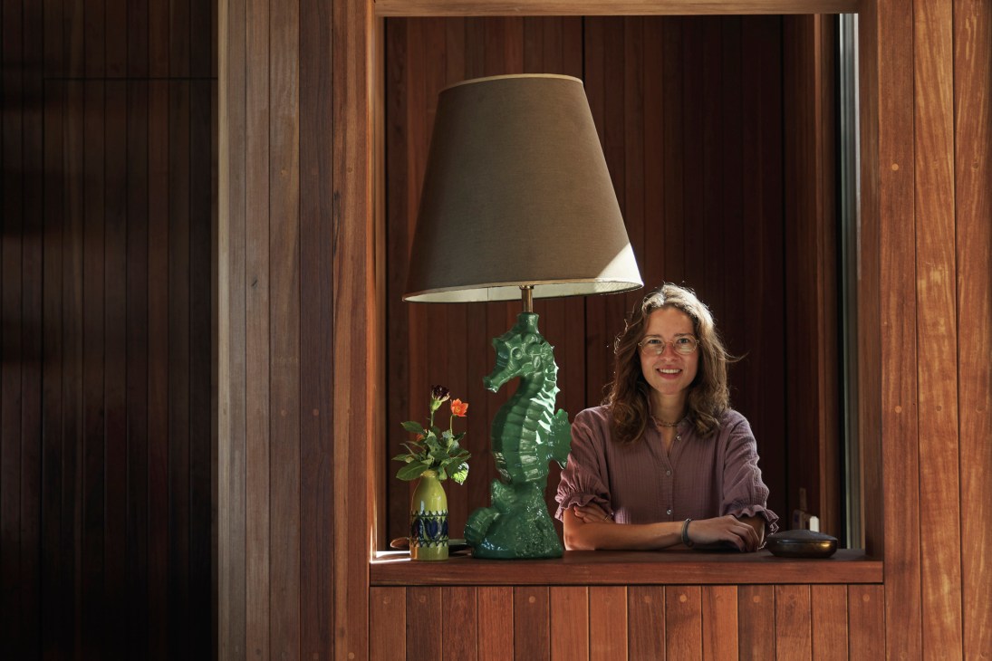 Woman smiling at desk with green seahorse lamp and potted flower in wooden-framed alcove.