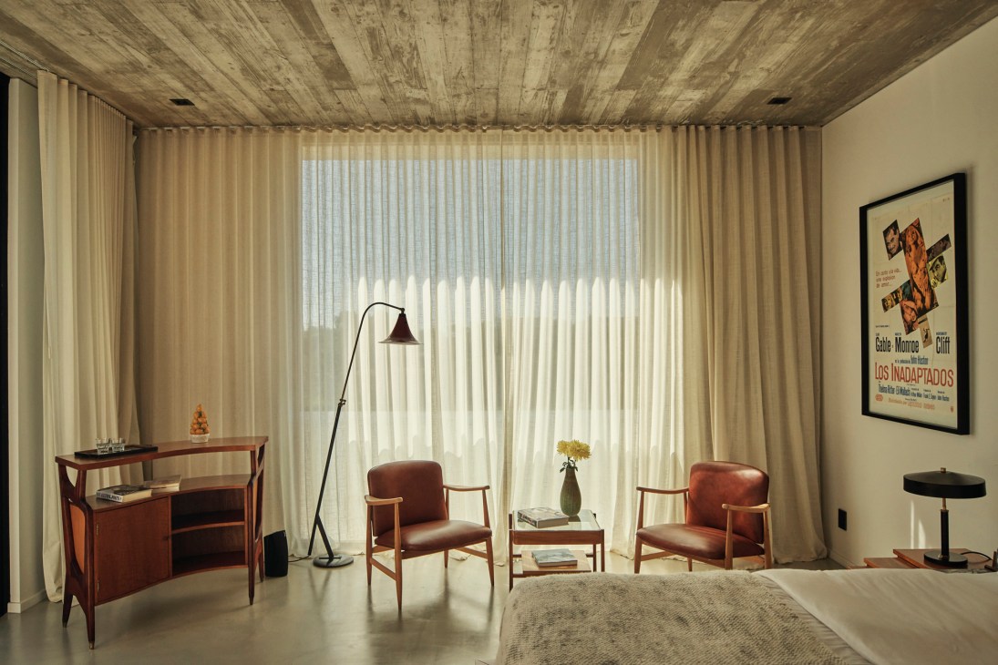 Mid-century modern bedroom at Posada Ayana with rust-colored leather chairs, wooden desk, and merino wool blanket on bed.