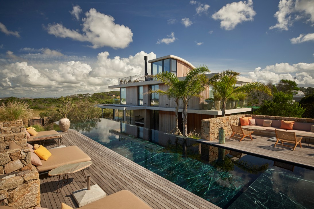 Modern two-story house with saltwater pool and wooden deck overlooking coastal landscape at Posada Ayana.
