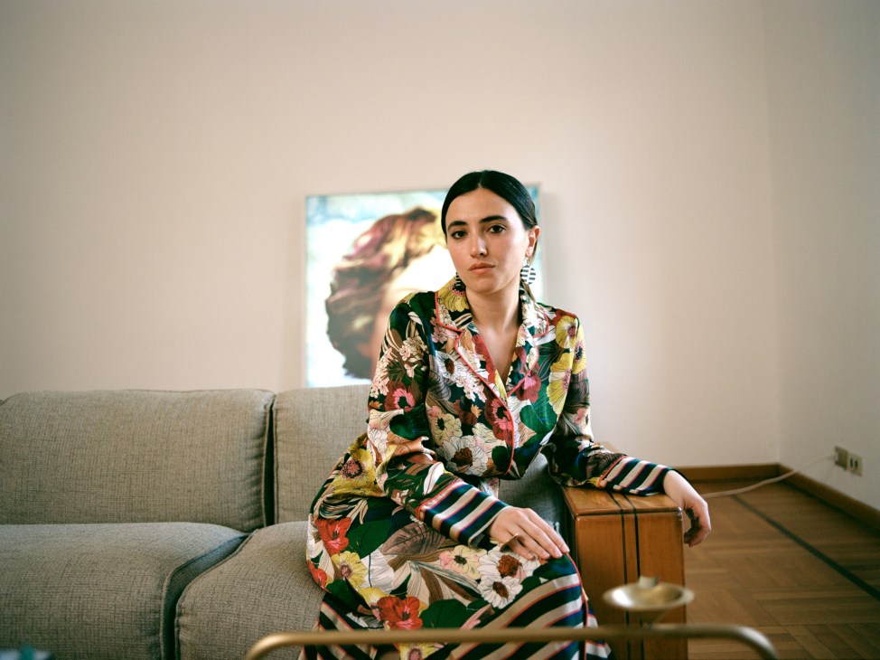 Joy Herro, co-founder of The Great Design Disaster, sits on a beige sofa wearing a colorful floral blazer with striped sleeves.