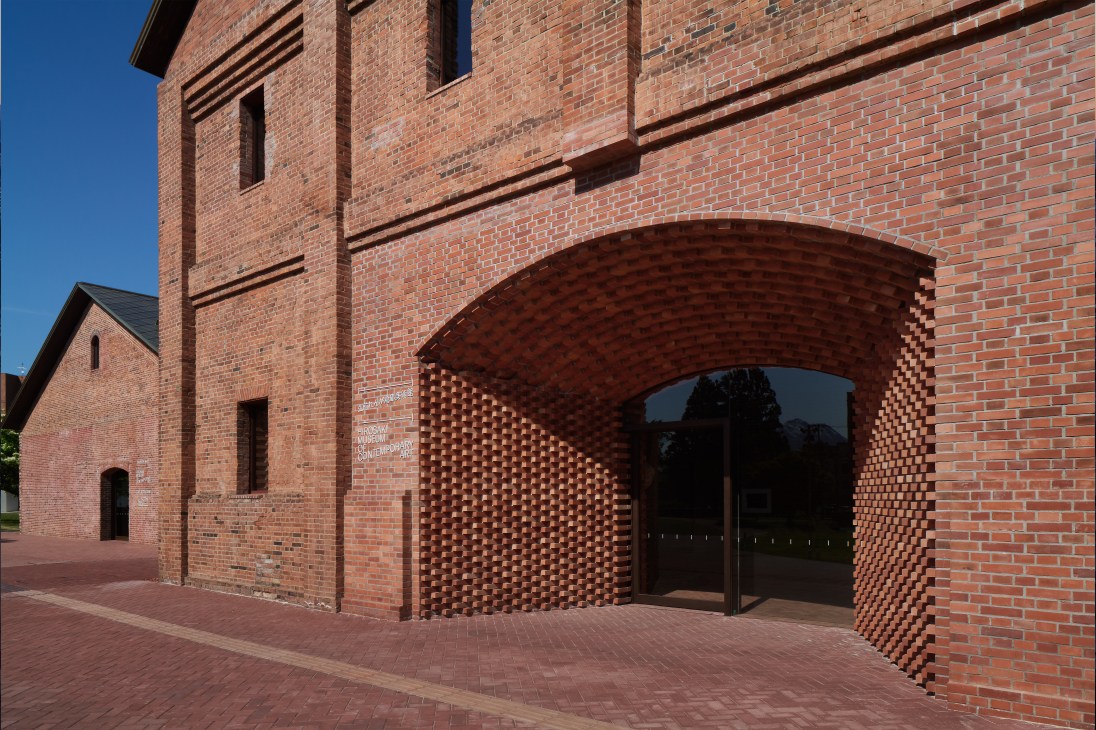 Red brick museum building with arched entrance and detailed brickwork patterns against blue sky