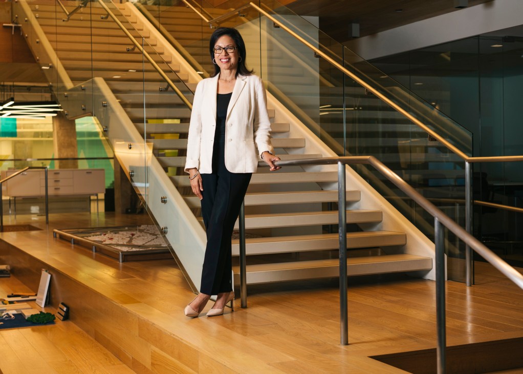 Diane Hoskins stands on wooden stairs in a modern office building with glass railings