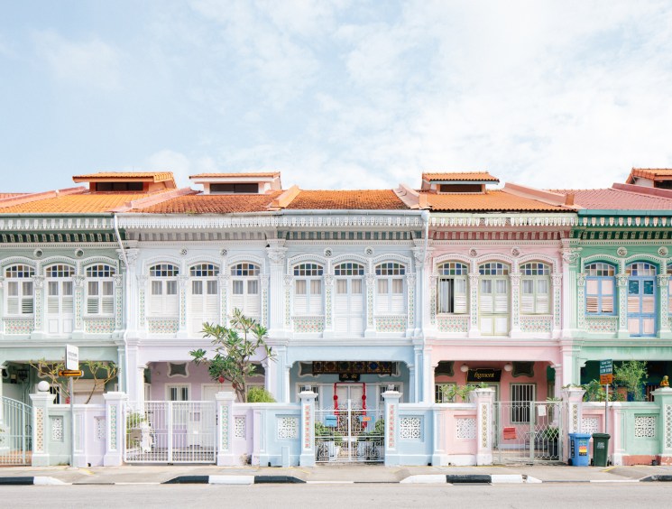 Colorful Peranakan-style shophouses with ornate facades and terracotta tile roofs line a street