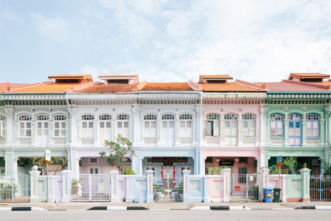 Colorful Peranakan-style shophouses with ornate facades and terracotta tile roofs line a street