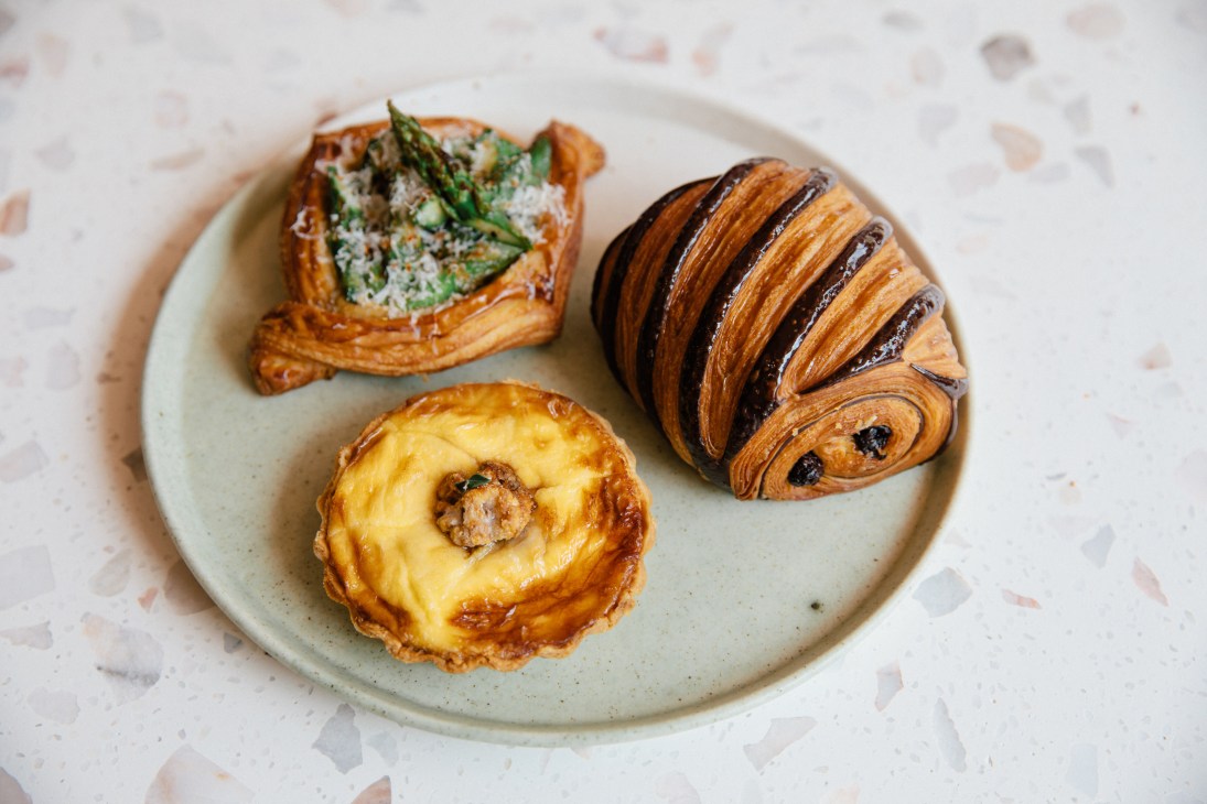 Three pastries on a white ceramic plate including a savory tart with greens and two sweet pastries