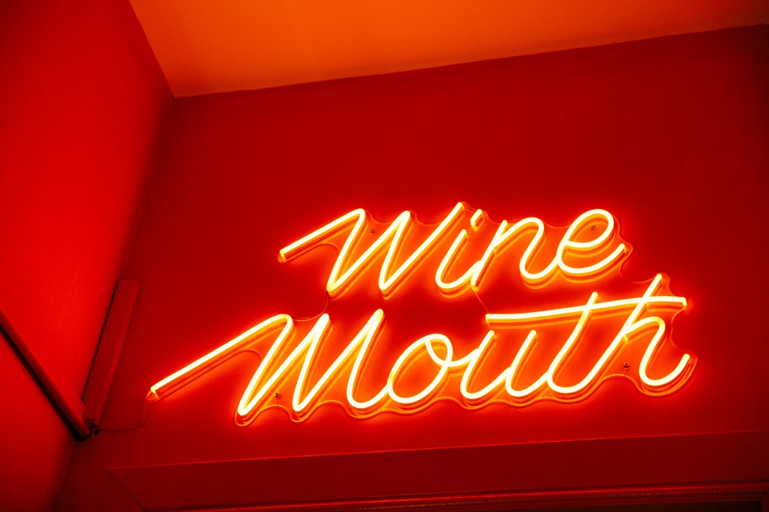 Glowing orange neon sign reading "Wine Mouth" on red wall