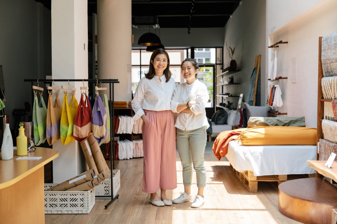 Two women standing together in a modern retail store with clothing racks and home goods displays