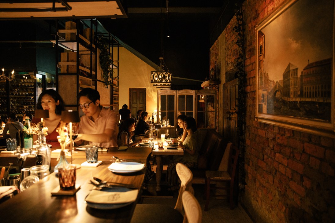 Dimly lit restaurant interior with diners at candlelit tables, exposed brick walls and warm ambient lighting