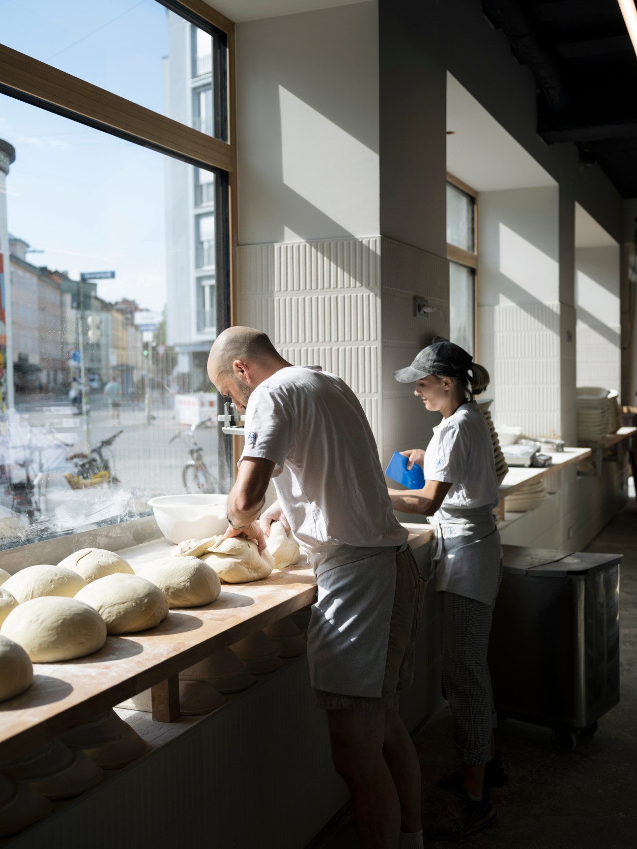 Two bakers working with bread dough at a wooden table in Julius Brantner Brothandwerk bakery in Munich
