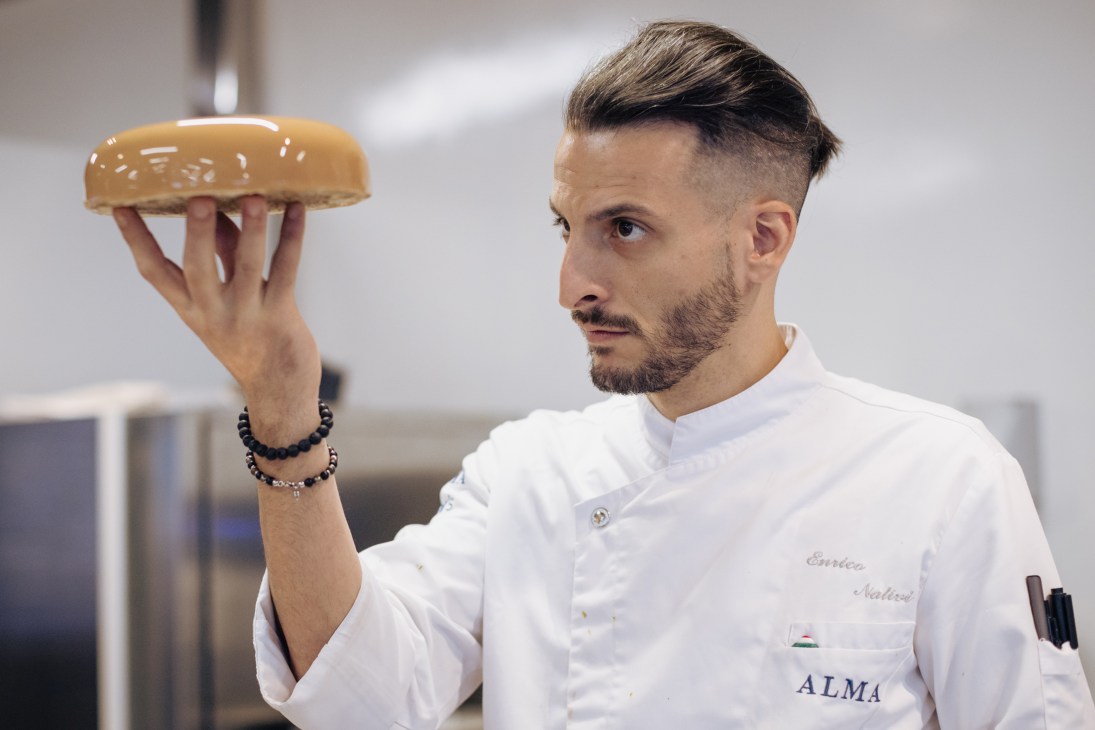 Chef in white uniform holding up a bread roll at The Food School in Bangkok.