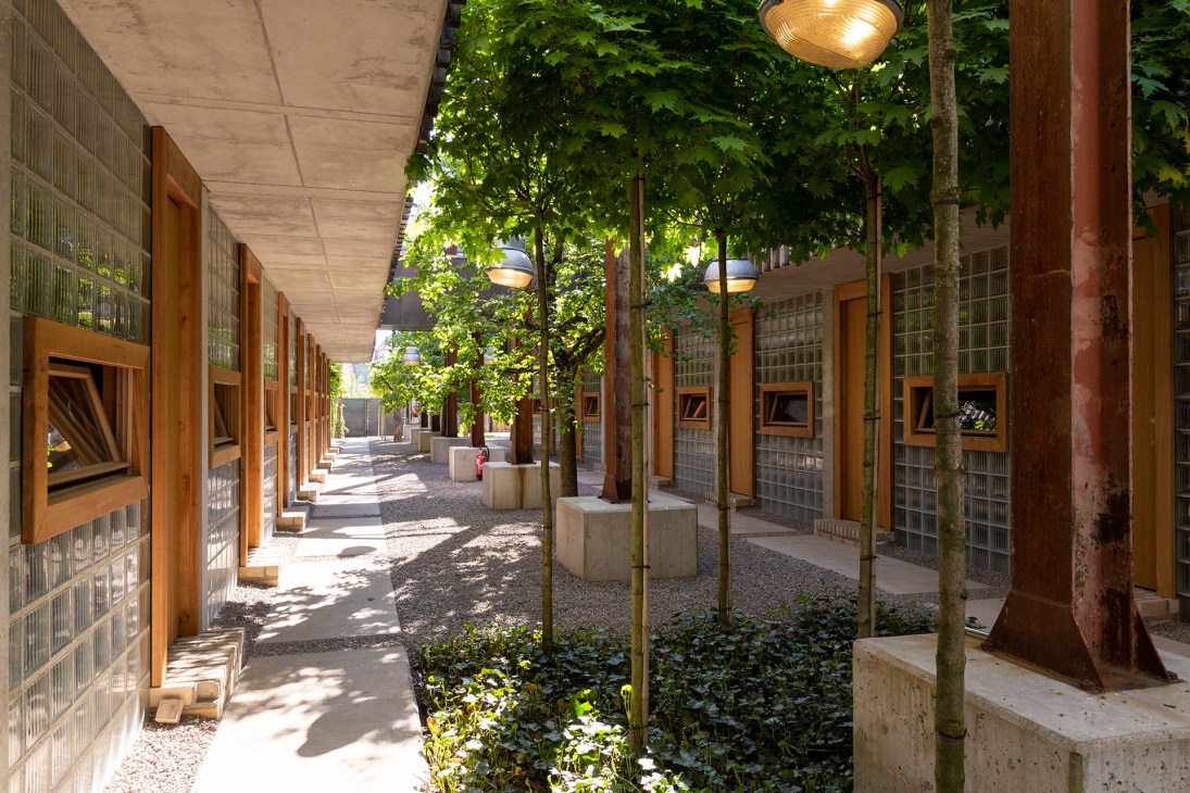 Modern hotel courtyard with wooden walkways, glass block walls, trees and hanging lights at Graace Luxembourg