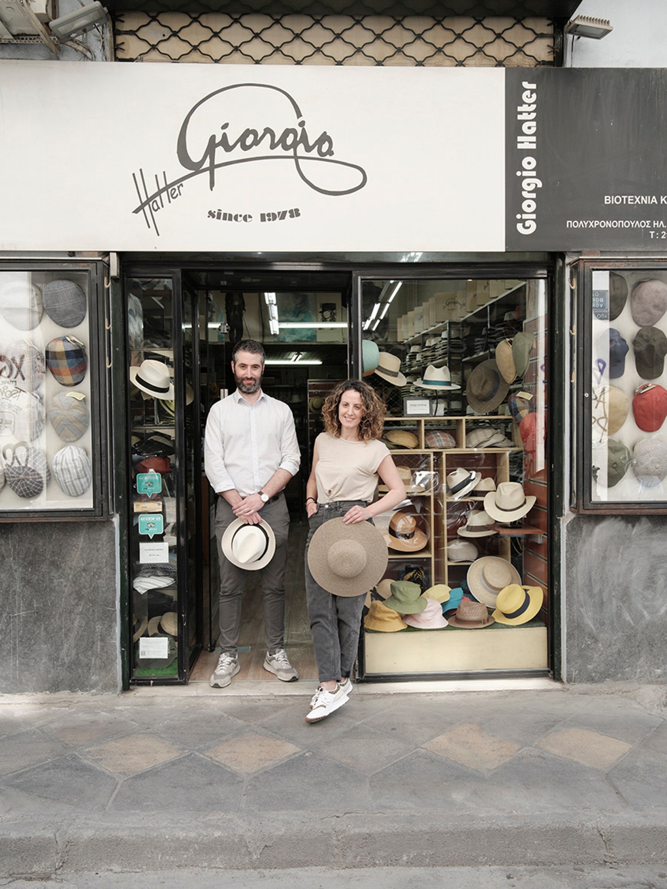 George and Vasiliki Polychronopoulos standing in doorway of Giorgio Hatter shop in Athens surrounded by hats