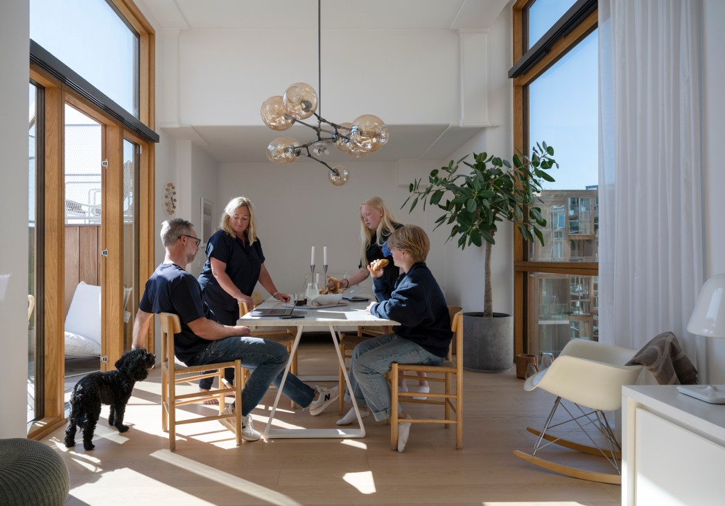Karl-Johan Bogefors and his family sitting at a table in their bright, modern apartment with floor-to-ceiling windows and wooden frames.