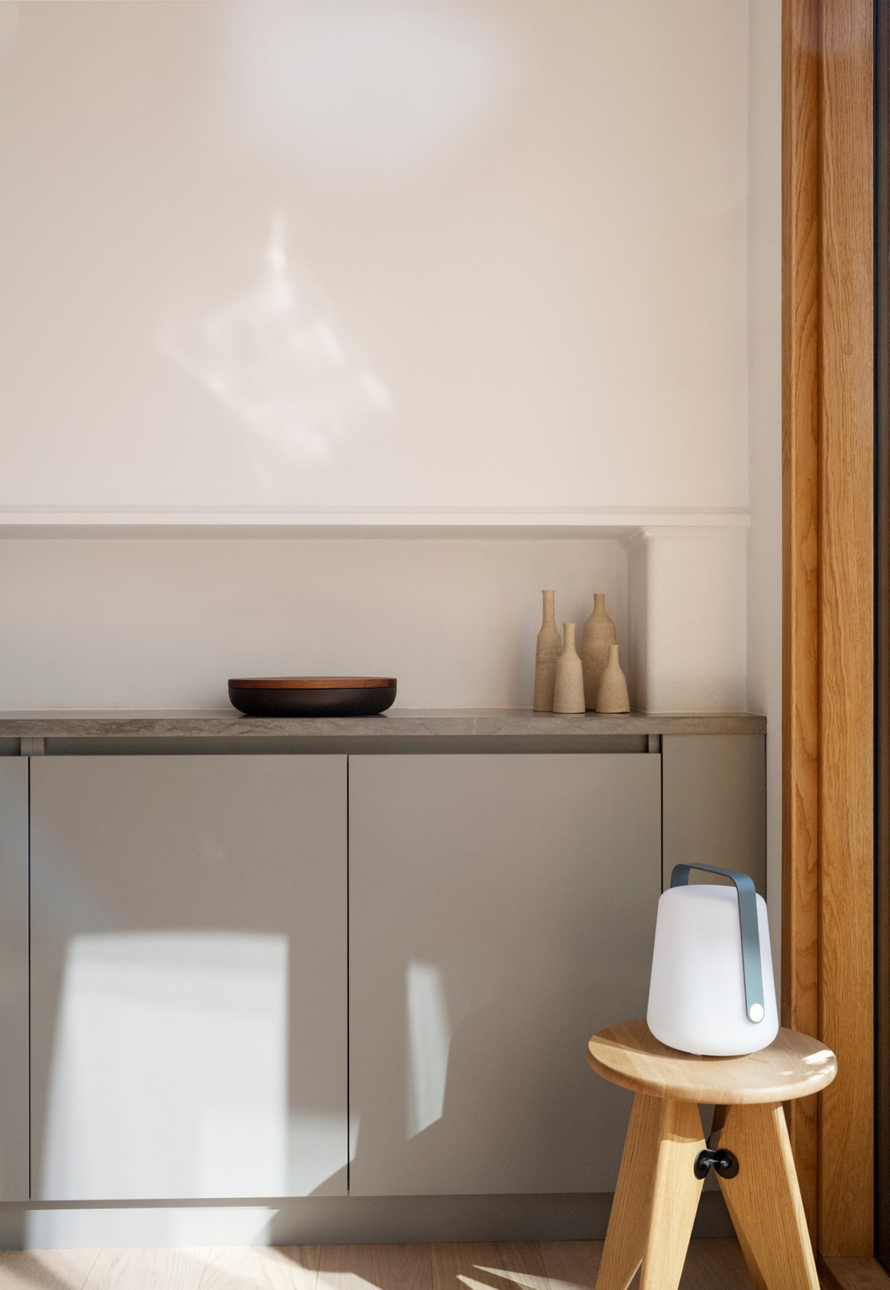 Minimalist apartment interior with wooden frame, concrete countertop, ceramic vessels and white portable device on wooden stool.