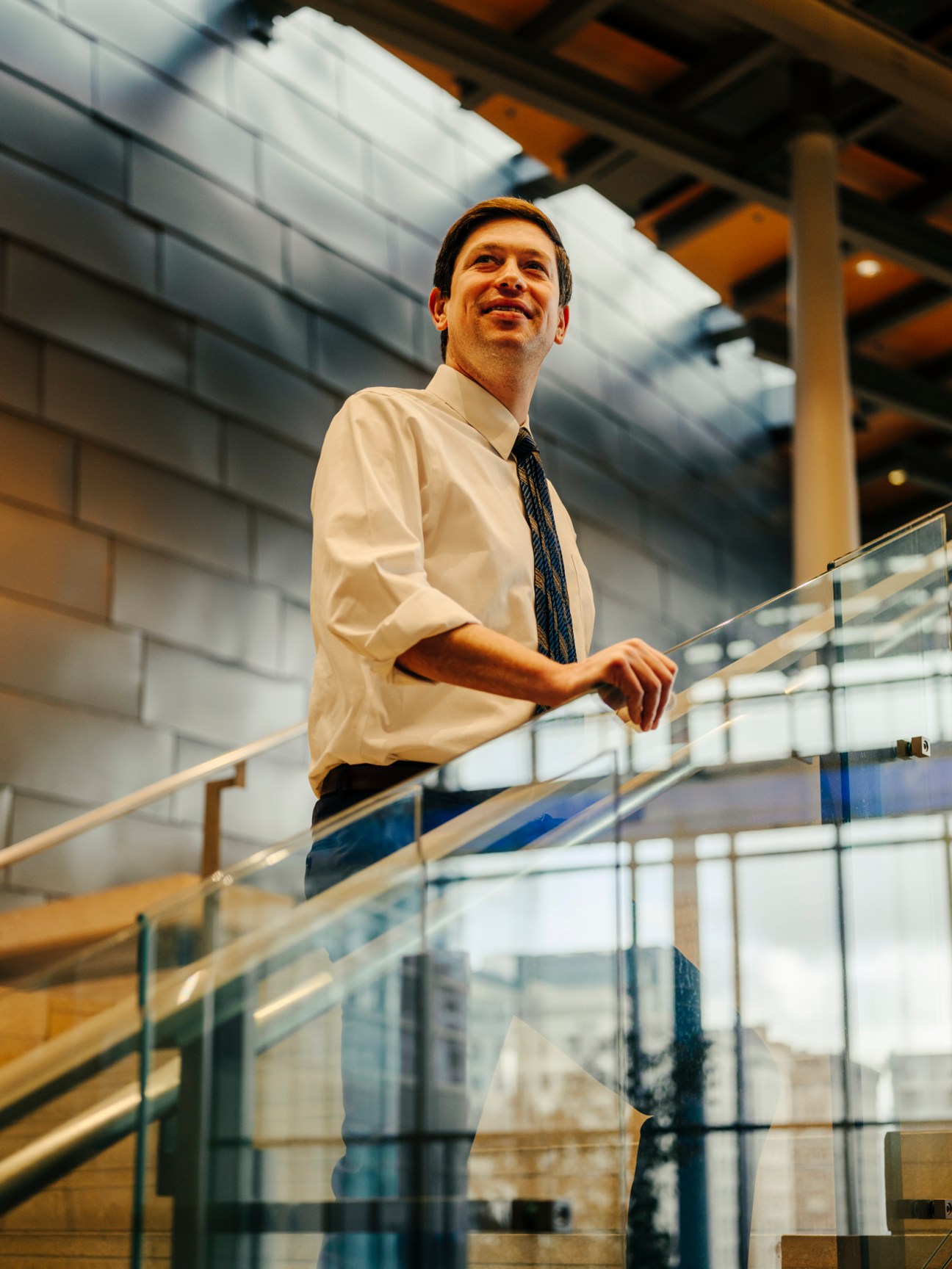 Council member Dan Strauss in white dress shirt and tie standing on balcony in modern building interior