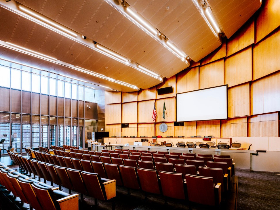 Interior view of Seattle City Council chambers with tiered seating facing curved dais and wood-paneled walls