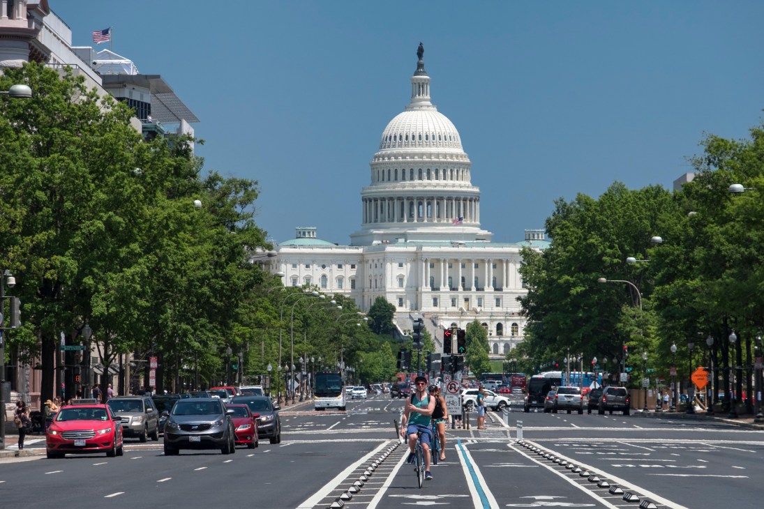 Street view of the US Capitol building with cyclist in bike lane and cars on Pennsylvania Avenue