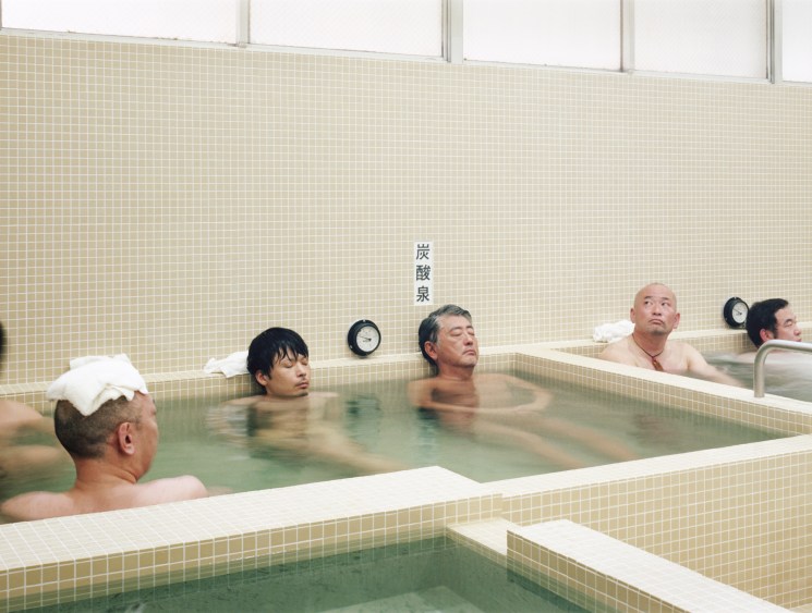 Men relaxing in traditional Japanese sento bathhouse with tiled walls and hot spring water