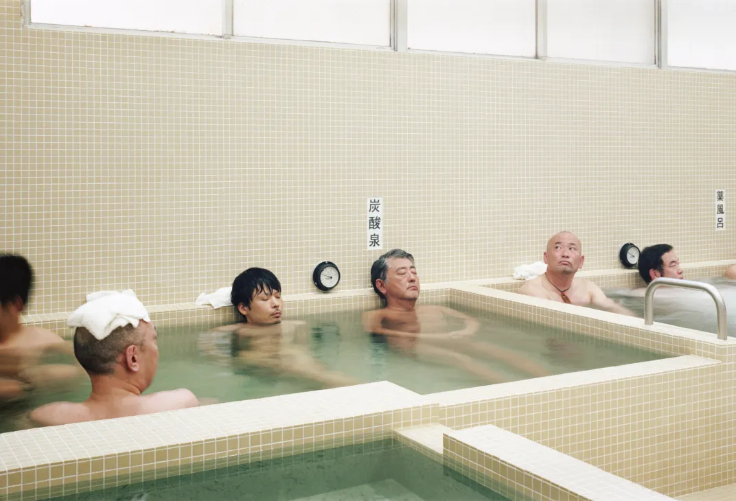 Men relaxing in traditional Japanese sento bathhouse with tiled walls and hot spring water