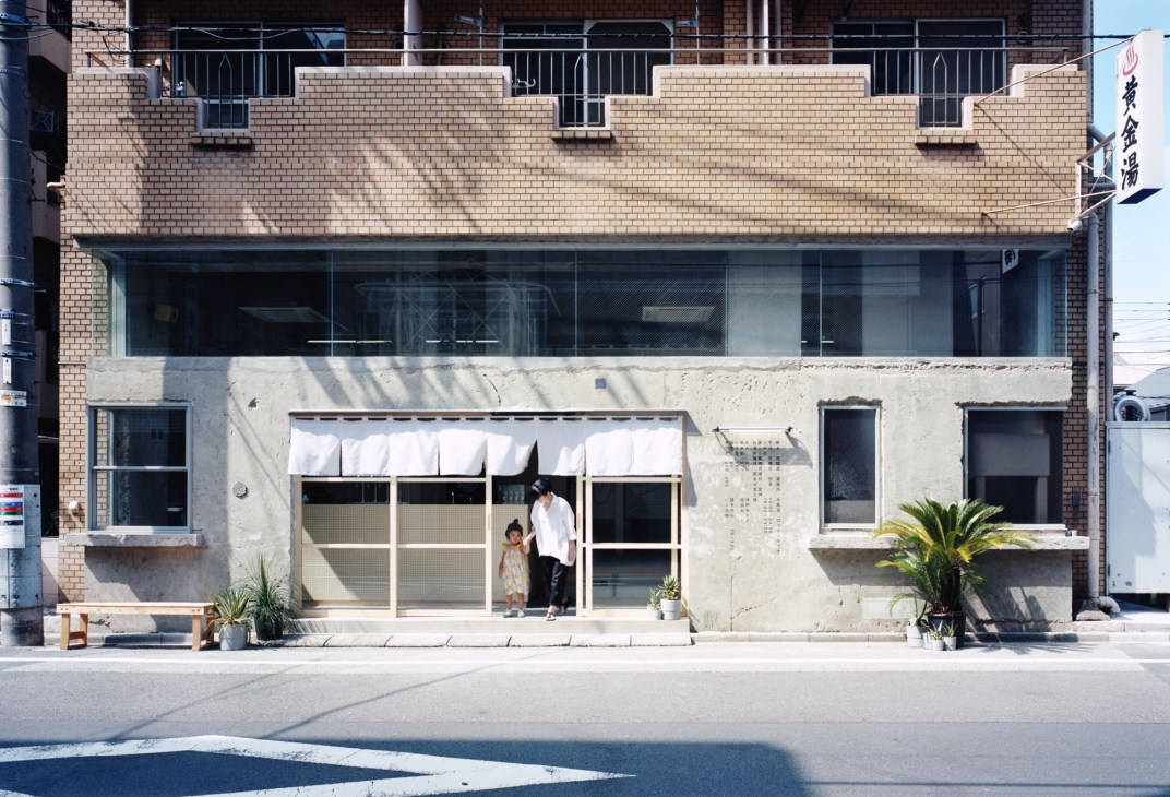 Exterior view of renovated Kogane-yu sento bathhouse with concrete facade, glass windows, and people at entrance