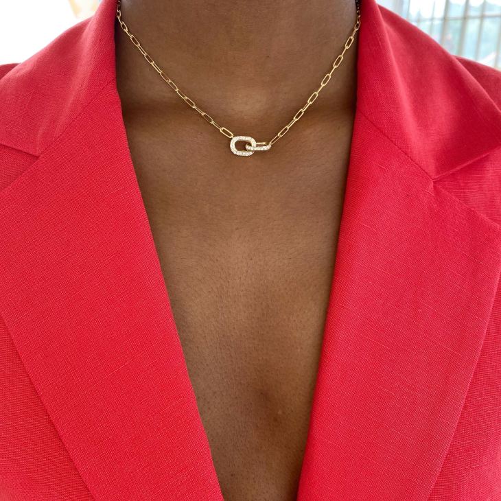Close-up of person wearing gold chain necklace with diamond-encrusted pendant against red blazer