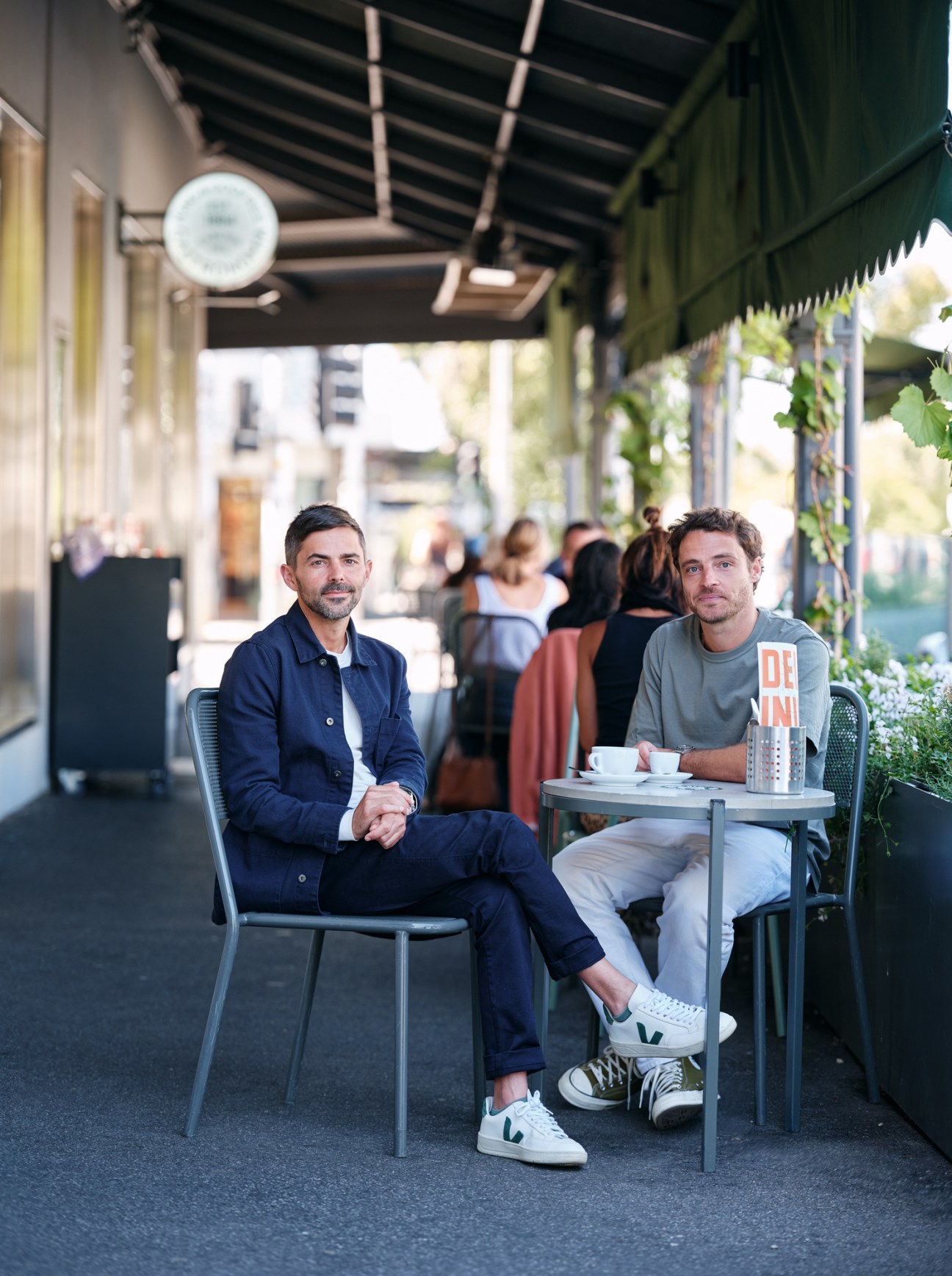 Two men sitting at outdoor cafe table under covered walkway