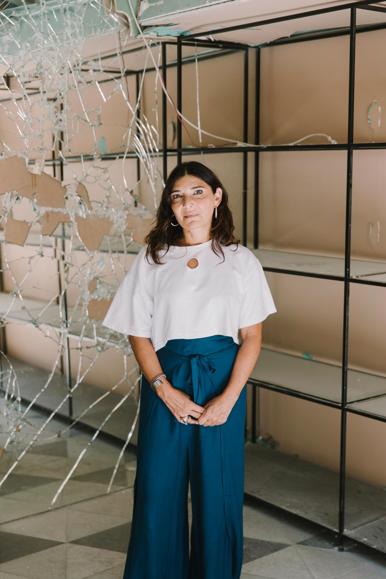 Designer Nada Debs standing in her damaged studio surrounded by broken mirrors and shattered design pieces