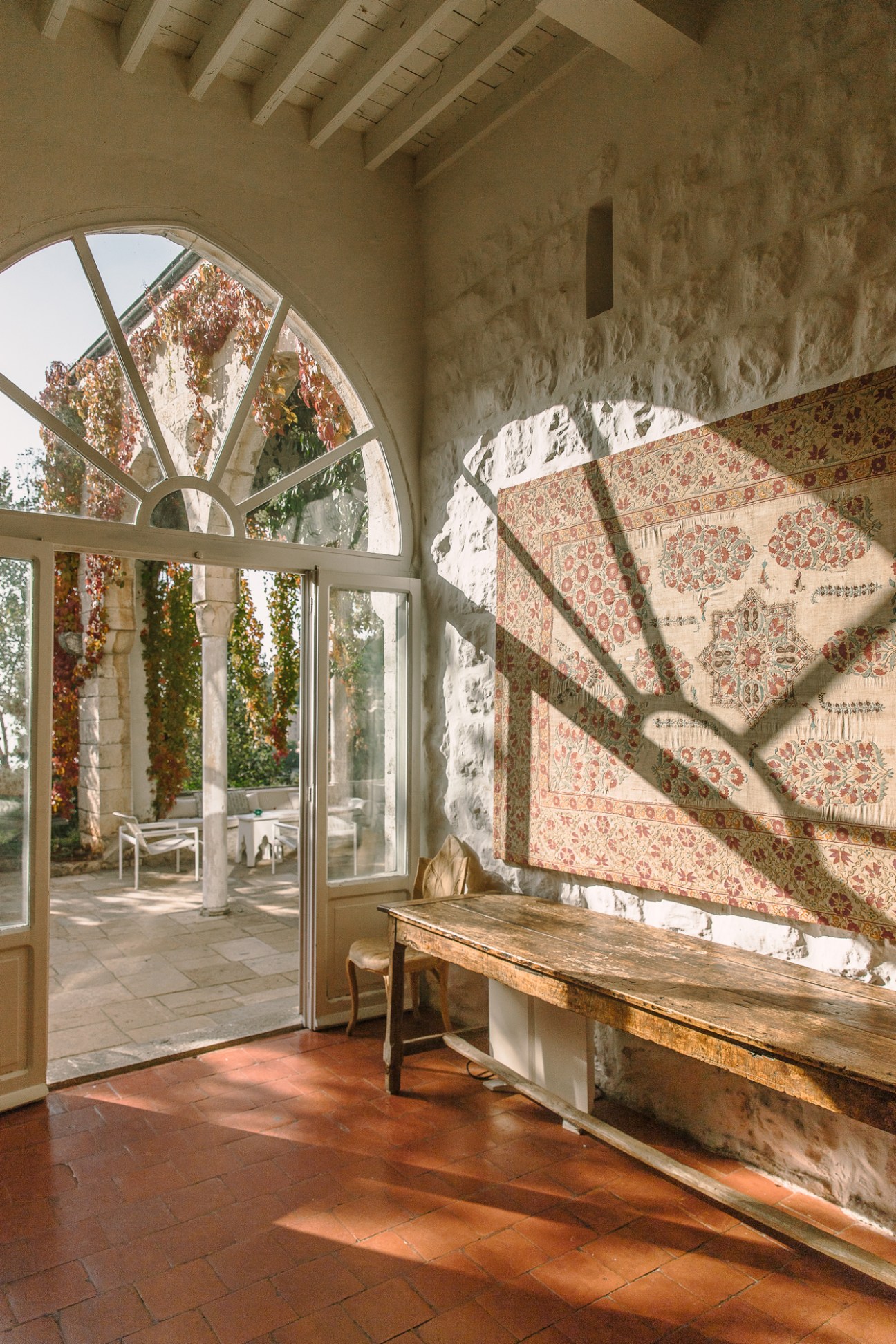 Bright entrance of Beit Trad with arched window, patterned textiles, and sunlit terracotta floor in Lebanon.