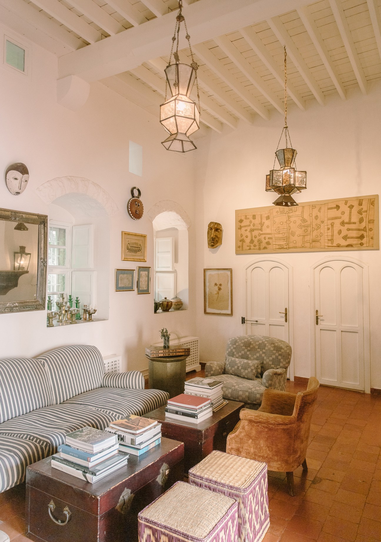 Sunlit interior salon with striped sofa, eclectic artwork, hanging lanterns, and cushioned seating at Beit Trad guesthouse.