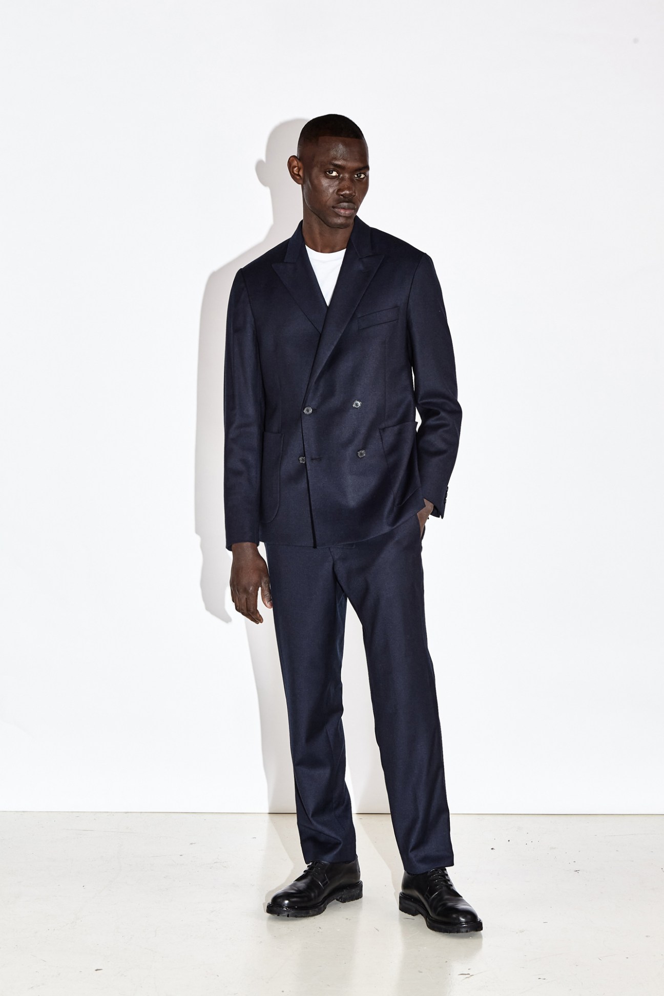 Model wearing navy double-breasted suit jacket with matching trousers, white t-shirt and black shoes